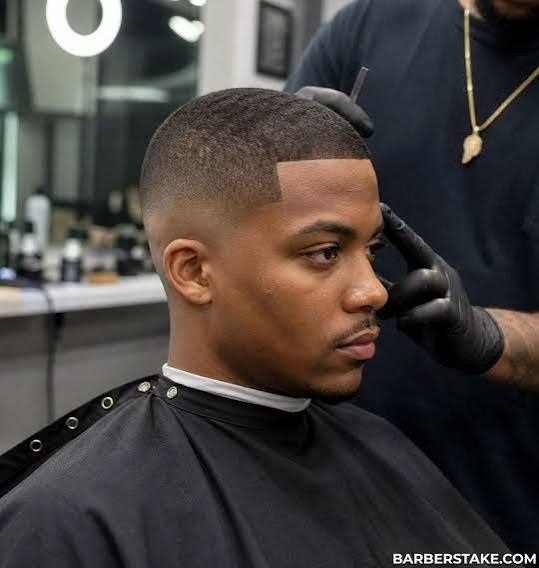 Barber shaping a client's fade with clippers in a dimly lit barbershop